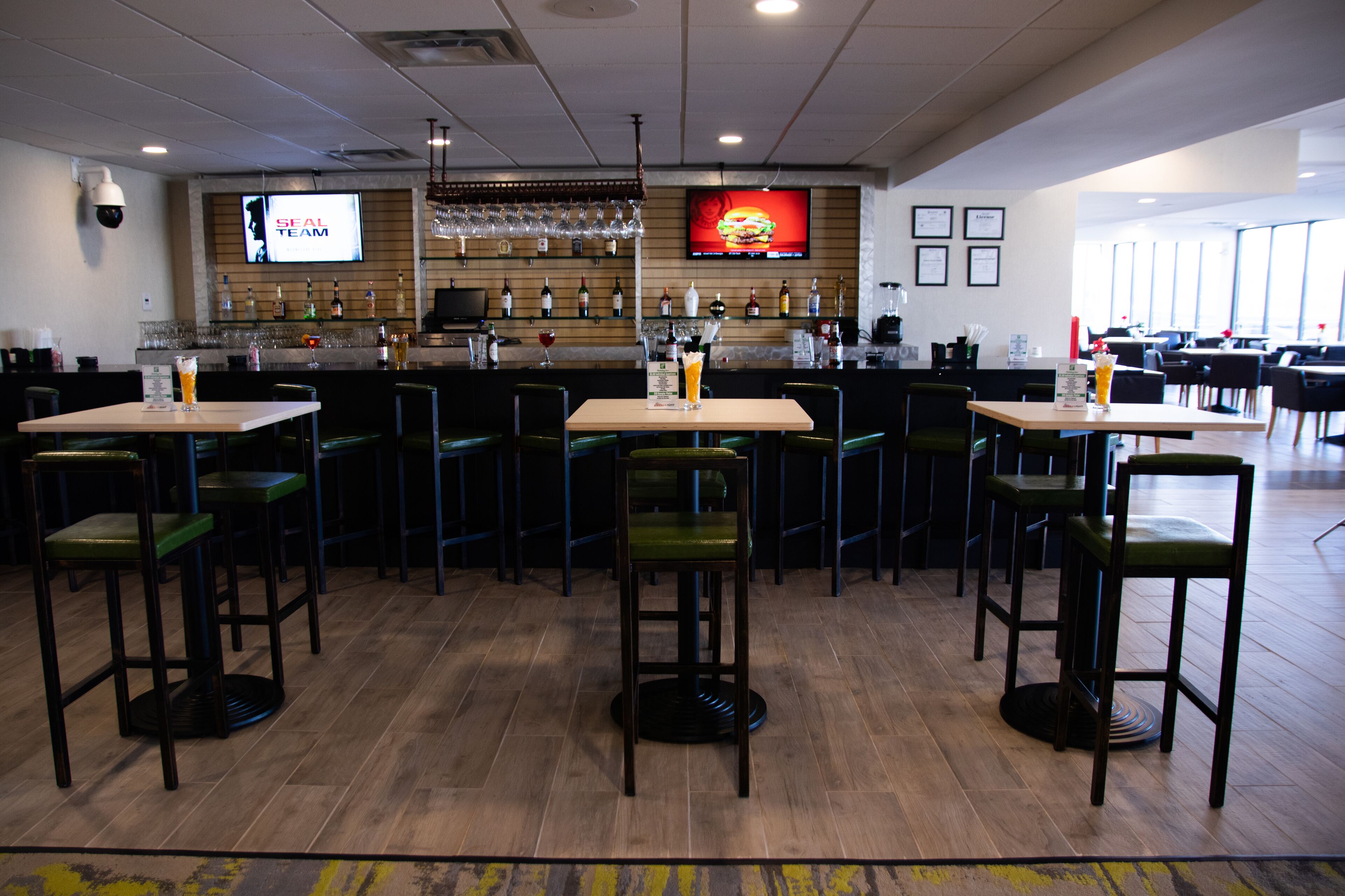 A restaurant with multiple tables and chairs, a bar area with a TV screen, and a wooden floor.