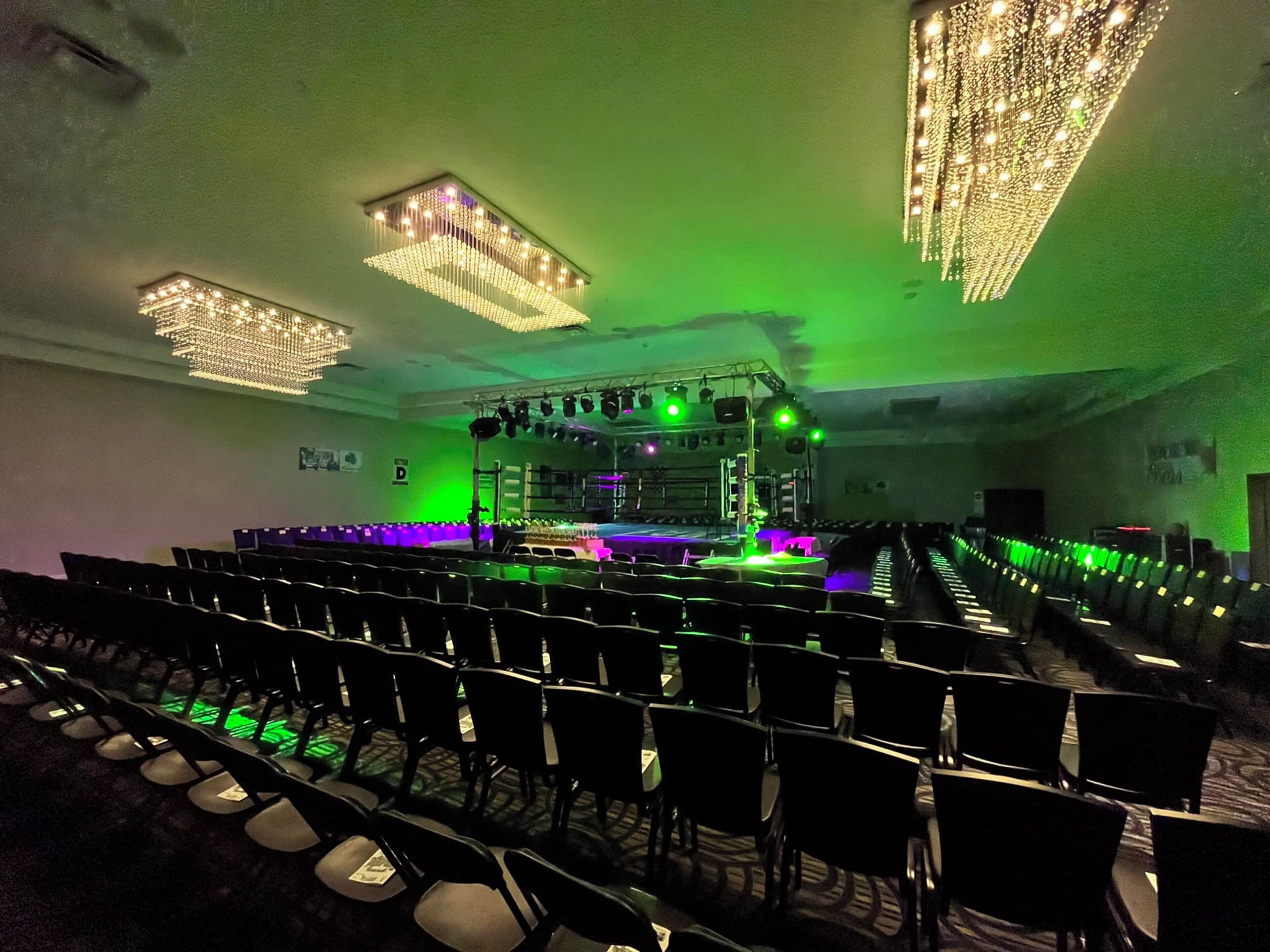 A conference room with rows of chairs, a stage with lighting equipment, and a green ambient light.