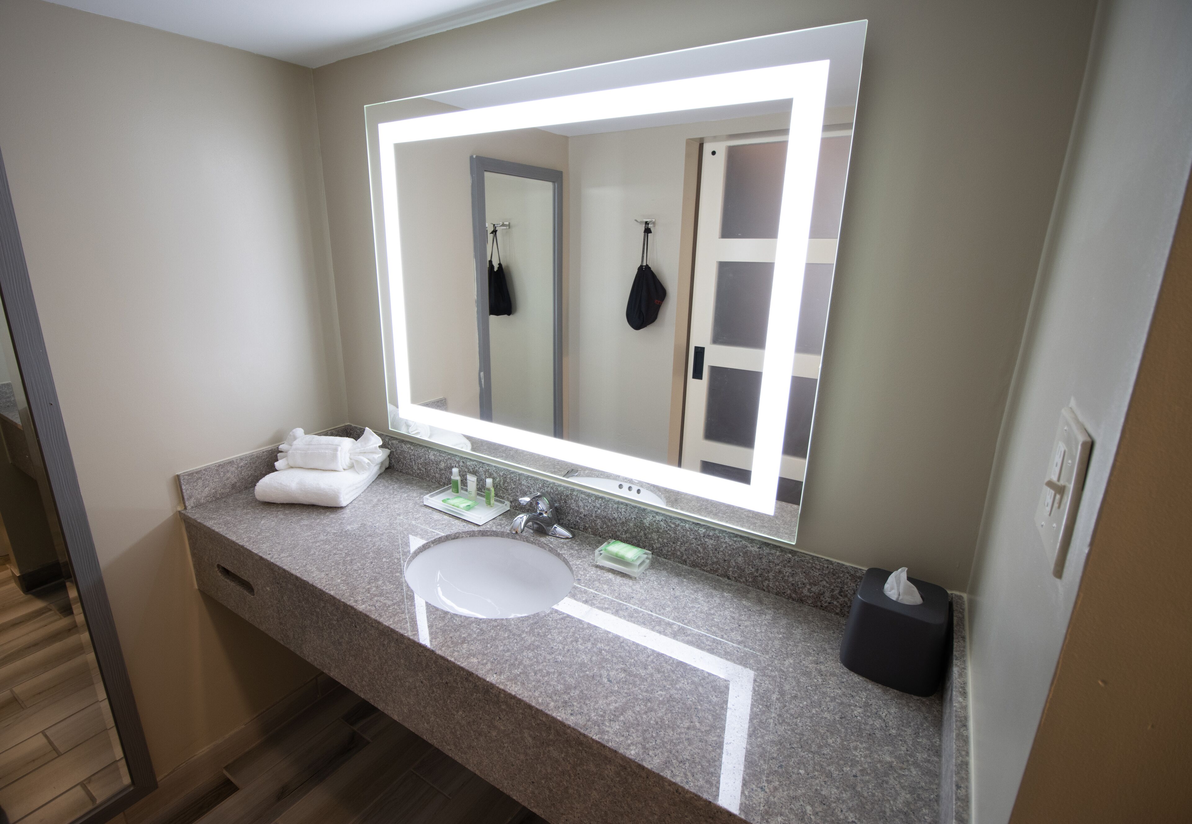 A bathroom with a large mirror, a sink, and a towel rack.
