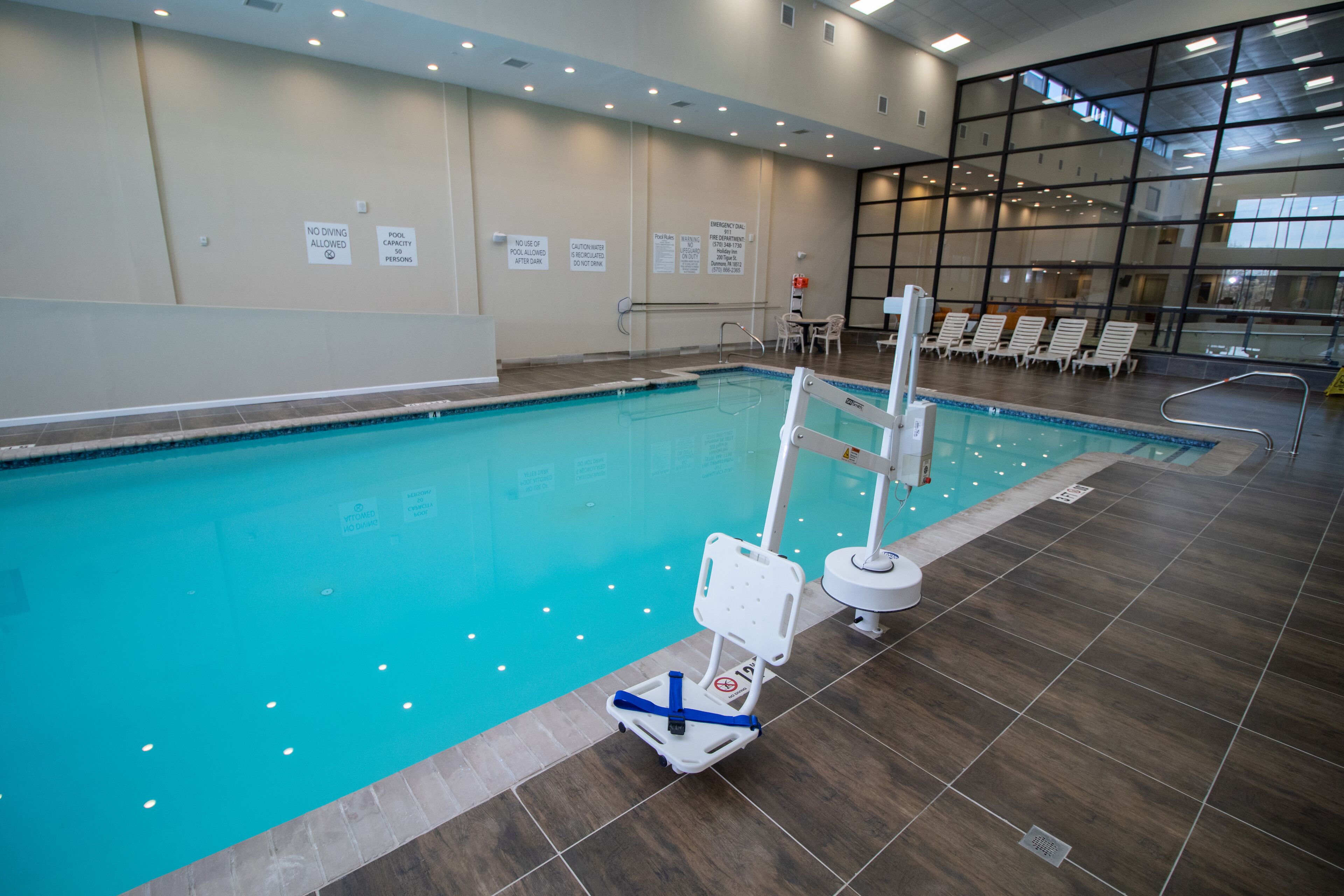 Una piscina interior con señalización clara, una silla de salvavidas y sillas de descanso.