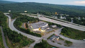 An aerial view of a commercial building with a parking lot, surrounded by greenery and connected to a highway.