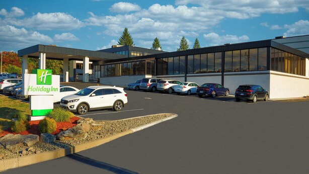 A Holiday Inn hotel with a modern building, a parking lot with several cars, and a clear sky.