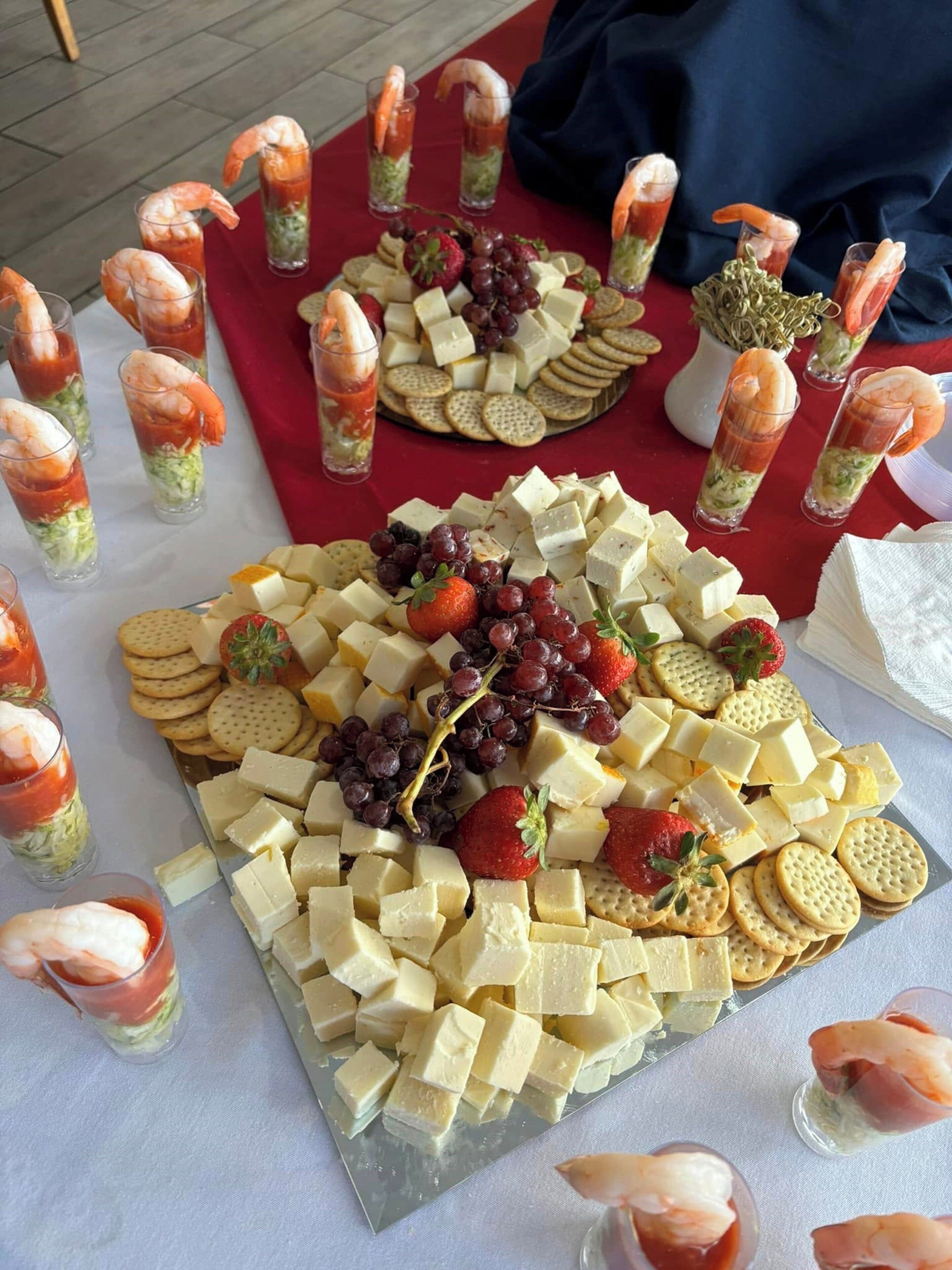 A table with a variety of cheeses, crackers, and shrimp cocktails.