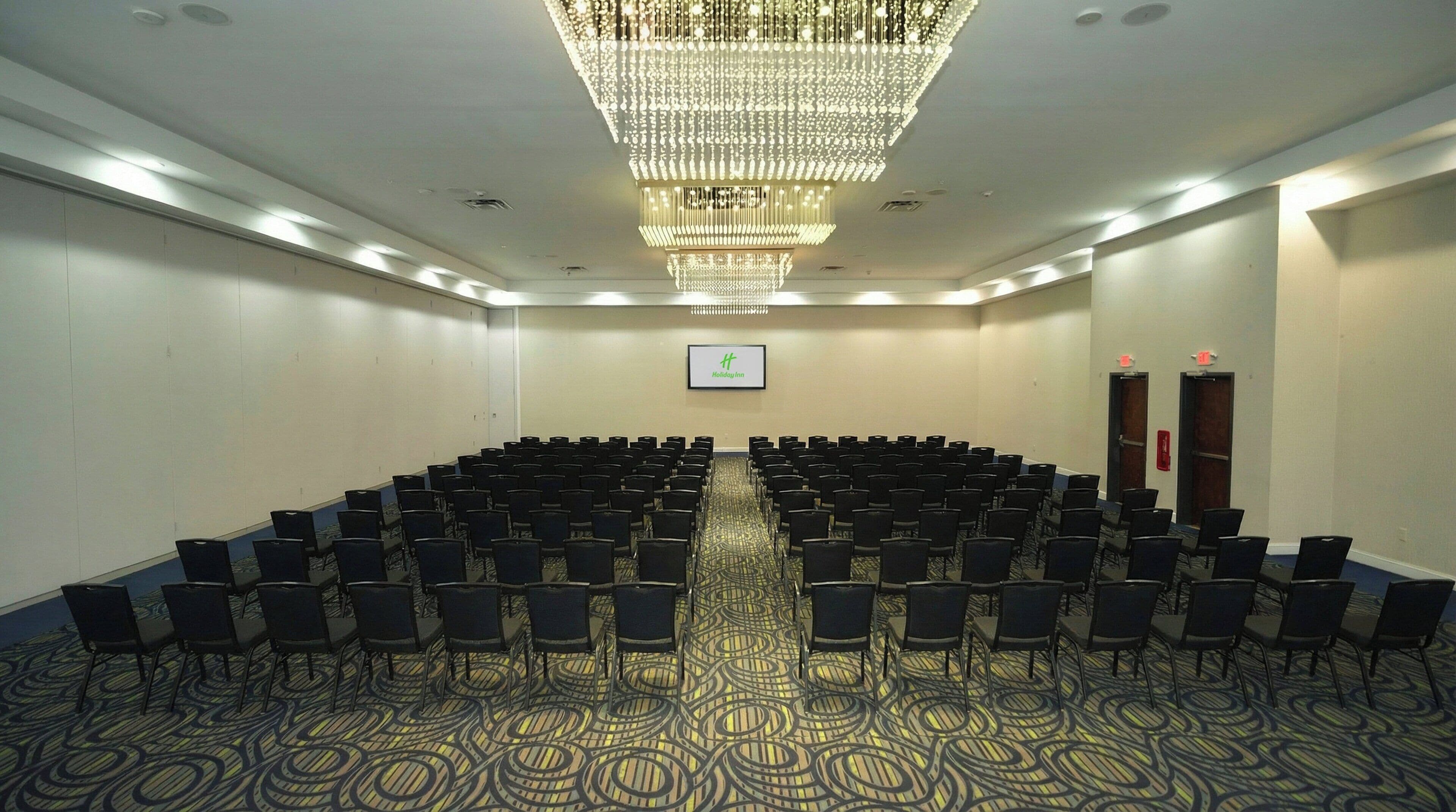 A conference room with rows of chairs, a chandelier, and a Holiday Inn sign on the wall.