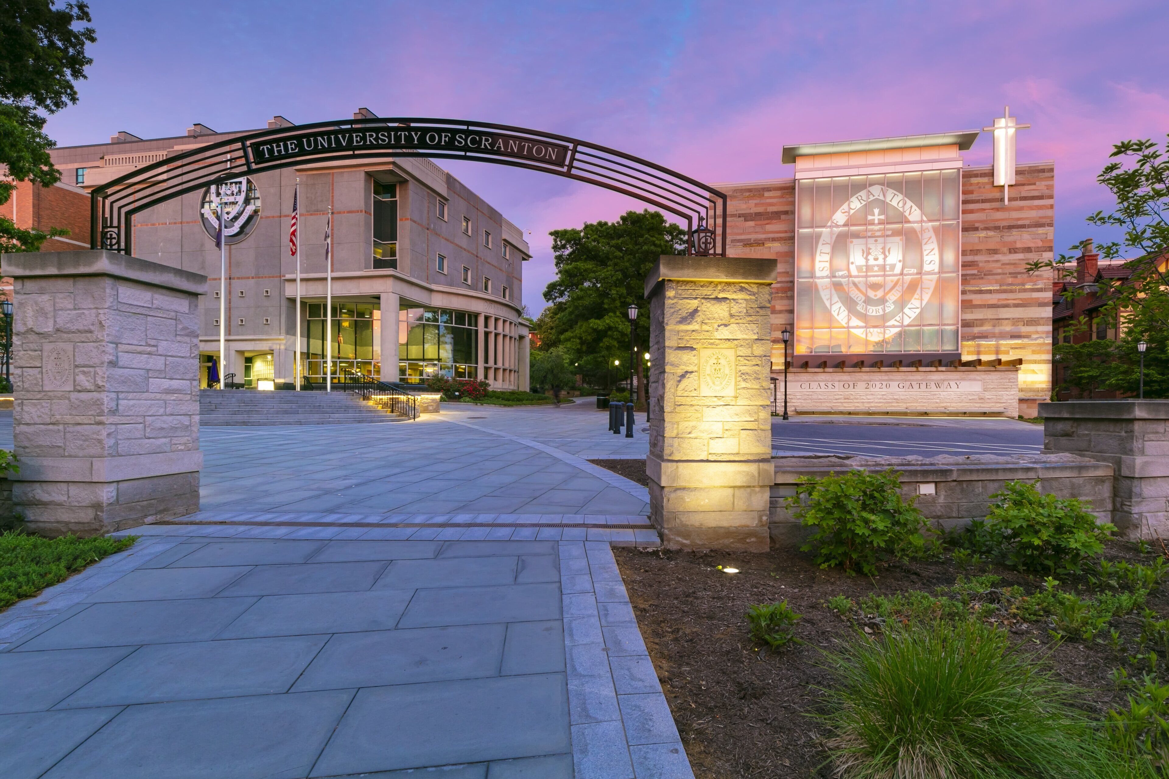 La entrada principal de la Universidad de Scranton, con un camino de piedra que lleva al edificio, un gran arco con el nombre de la universidad y un banderín para la promoción de 2020.