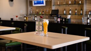 A bar area with a tall glass of beer, a menu stand, and shelves with bottles in the background.