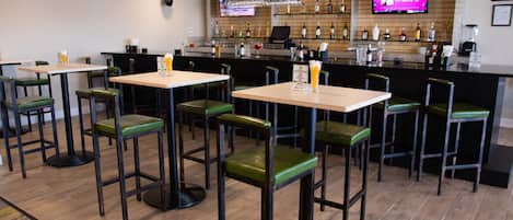 A restaurant with multiple bar stools and tables, a bar area with a TV screen, and a variety of bottles and glasses on shelves.