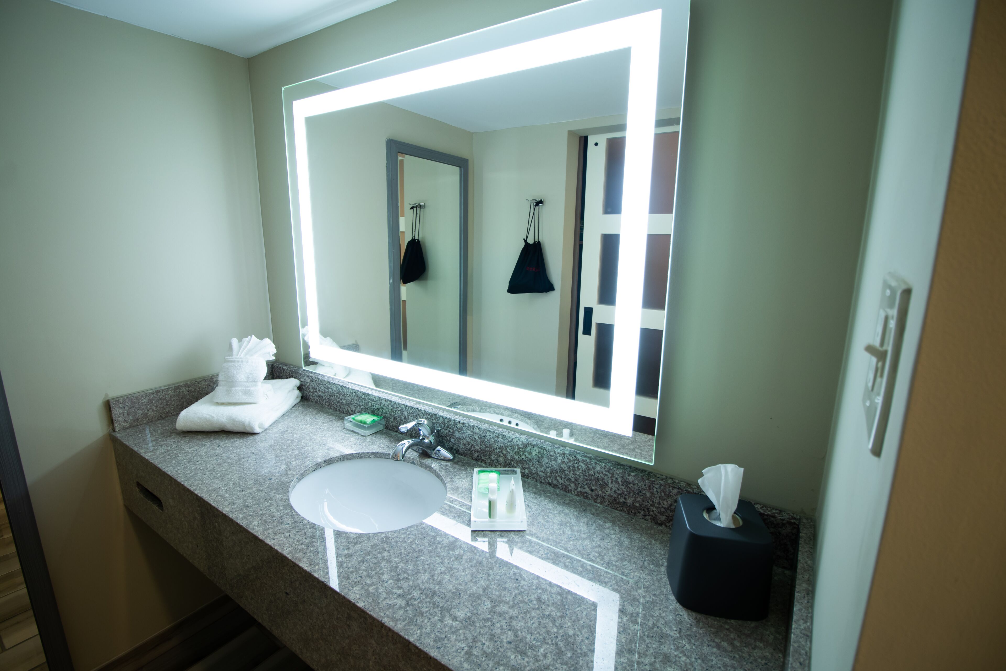 A bathroom with a large mirror, a sink, a towel rack, and a tissue dispenser.