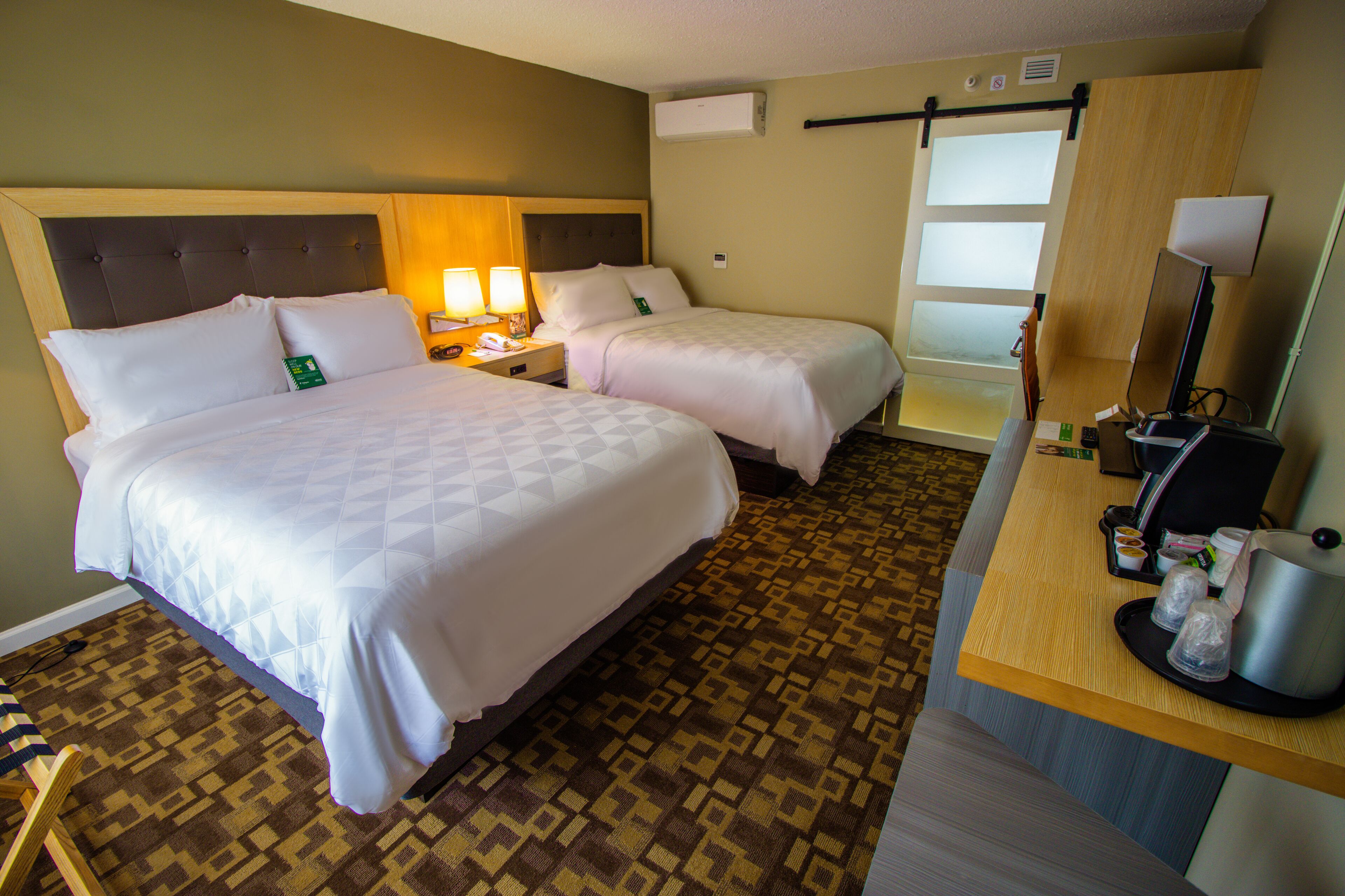 A hotel room with two beds, a desk, a chair, a coffee maker, and a mirror.