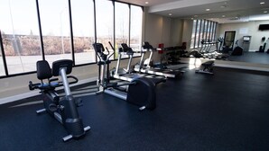 A gym with various exercise equipment, large windows, and a mirror on the wall.