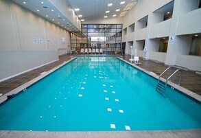 Una piscina interior con agua cristalina, rodeada de paredes con ventanas y señalización, y un suelo de baldosas.