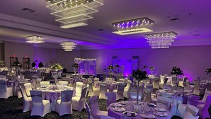 A banquet hall with round tables, white chairs, and chandeliers.