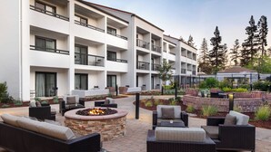 Un patio de hotel con mobiliario exterior, una zona de fogata y un área de piscina.