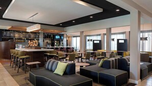 Un moderno vestíbulo de hotel con zona de bar, arreglos de asientos y un amplio ventanal que proporciona luz natural.