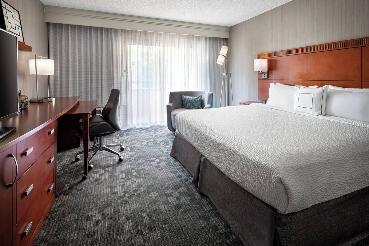 A hotel room with a large bed, a desk with a chair, a television, and a window with curtains.