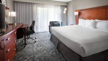 A hotel room with a large bed, a desk with a chair, a television, and a window with curtains.