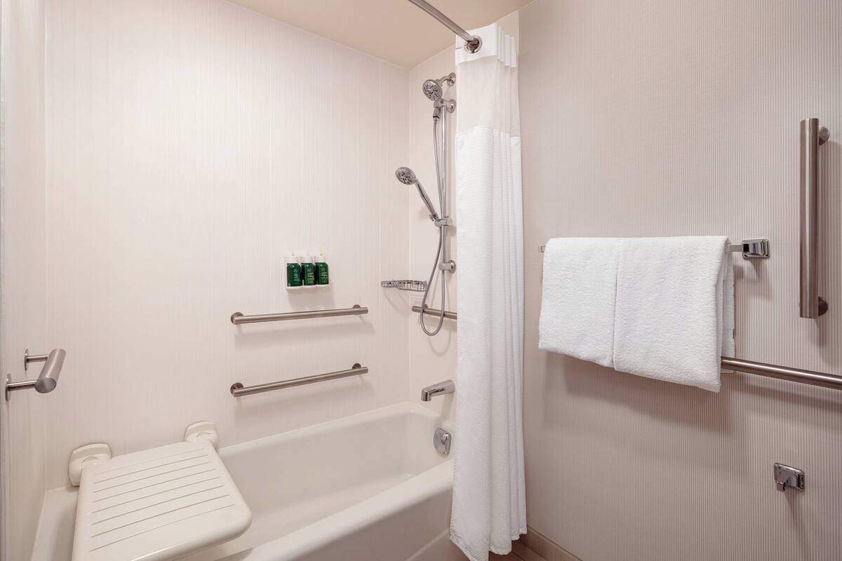A modern bathroom with a bathtub, shower, and handrails.