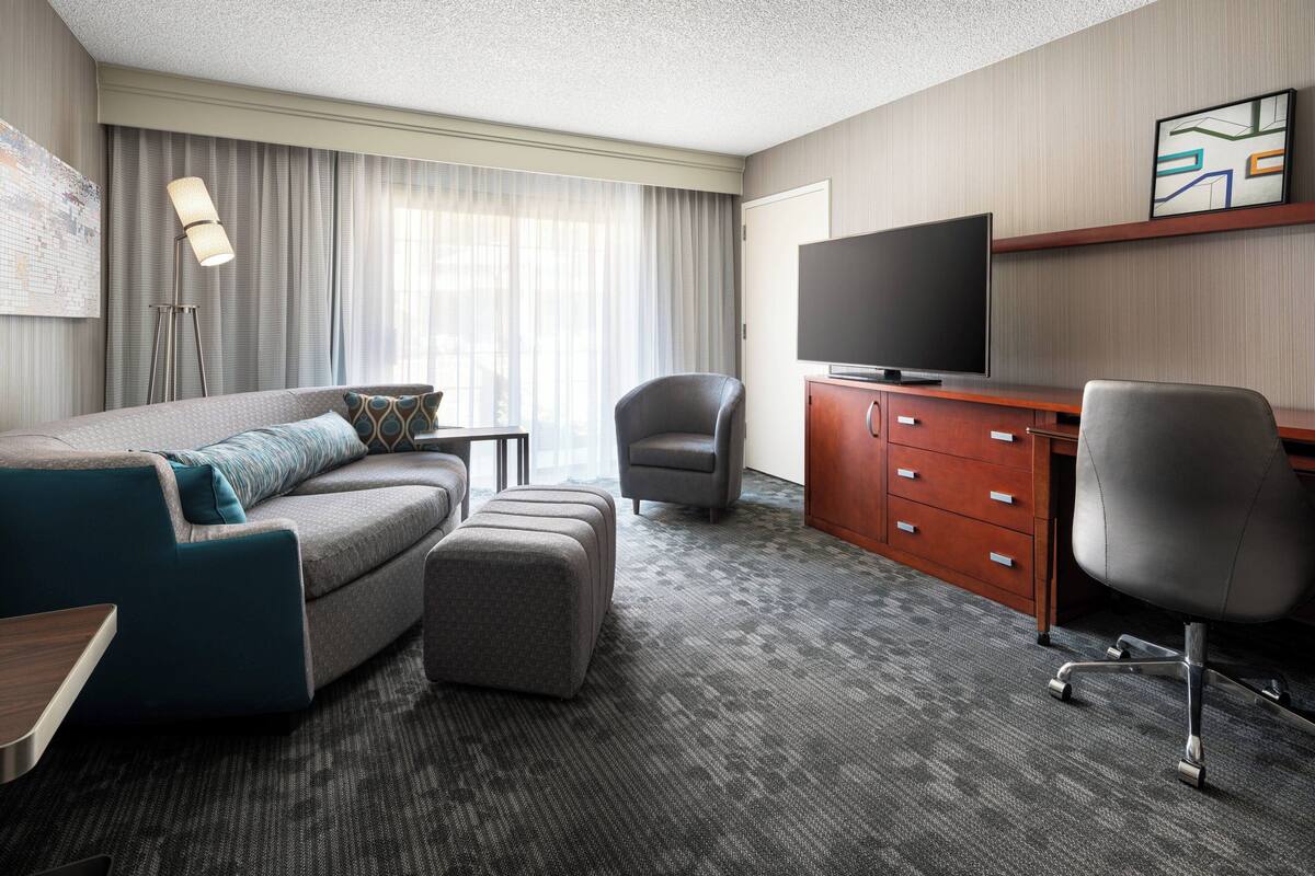 A hotel room with a sofa, ottoman, two chairs, a desk, a television, and a cabinet.