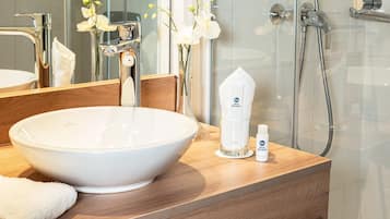 Une salle de bain avec un grand lavabo blanc, un miroir, une douche et un flacon de lotion.