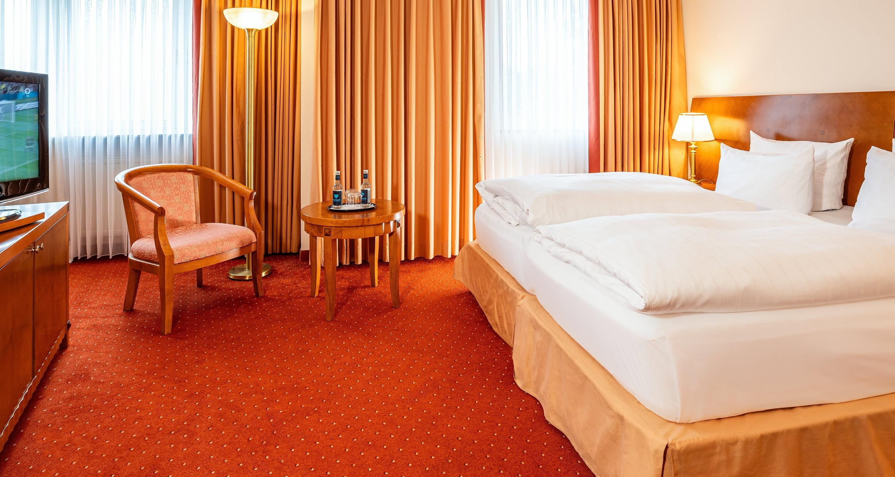Een hotelkamer met een bed, een stoel, een klein tafeltje met dienblad, een televisie en gordijnen.