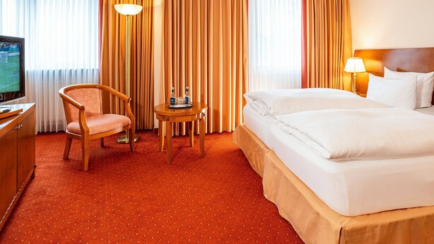 A hotel room with a bed, a chair, a small table with a tray, a TV, and curtains.