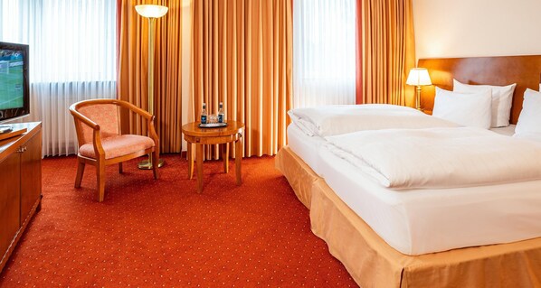 Una habitación de hotel con cama, una silla, una mesita con bandeja, televisión y cortinas.
