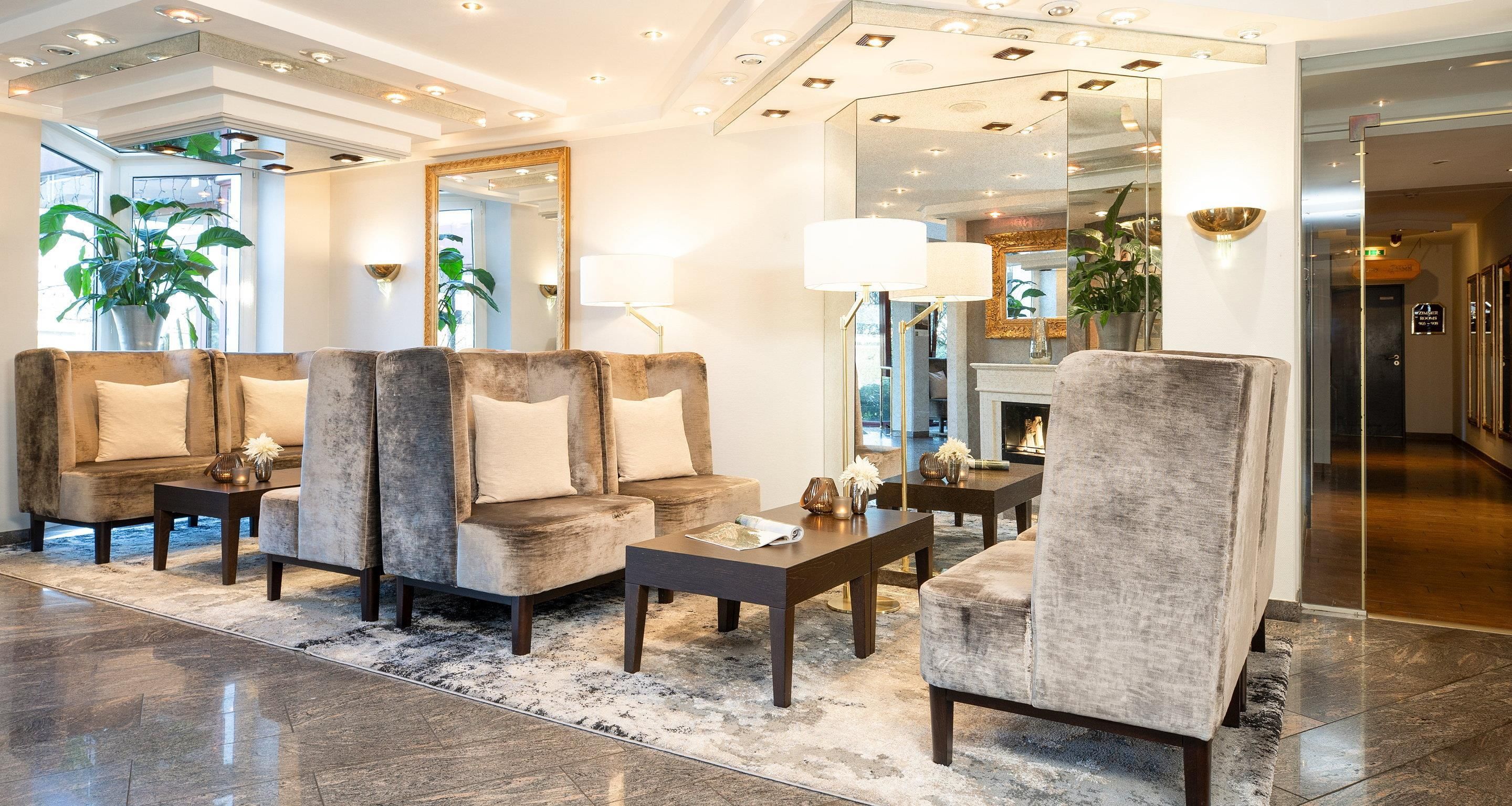 Een moderne lobby met een zithoek, een open haard en een grote spiegel die de ruimte weerspiegelt.
