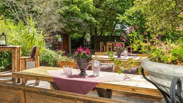An outdoor dining area with wooden tables, chairs, and potted plants.