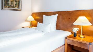 A hotel room with a wooden headboard, white bedding, two bedside lamps, and a framed picture on the wall.
