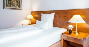 A hotel room with a wooden headboard, white bedding, two bedside lamps, and a framed picture on the wall.