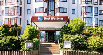 Entrada de un hotel con un cartel que dice 'Best Western', rodeada de vegetación y una escalera que sube.