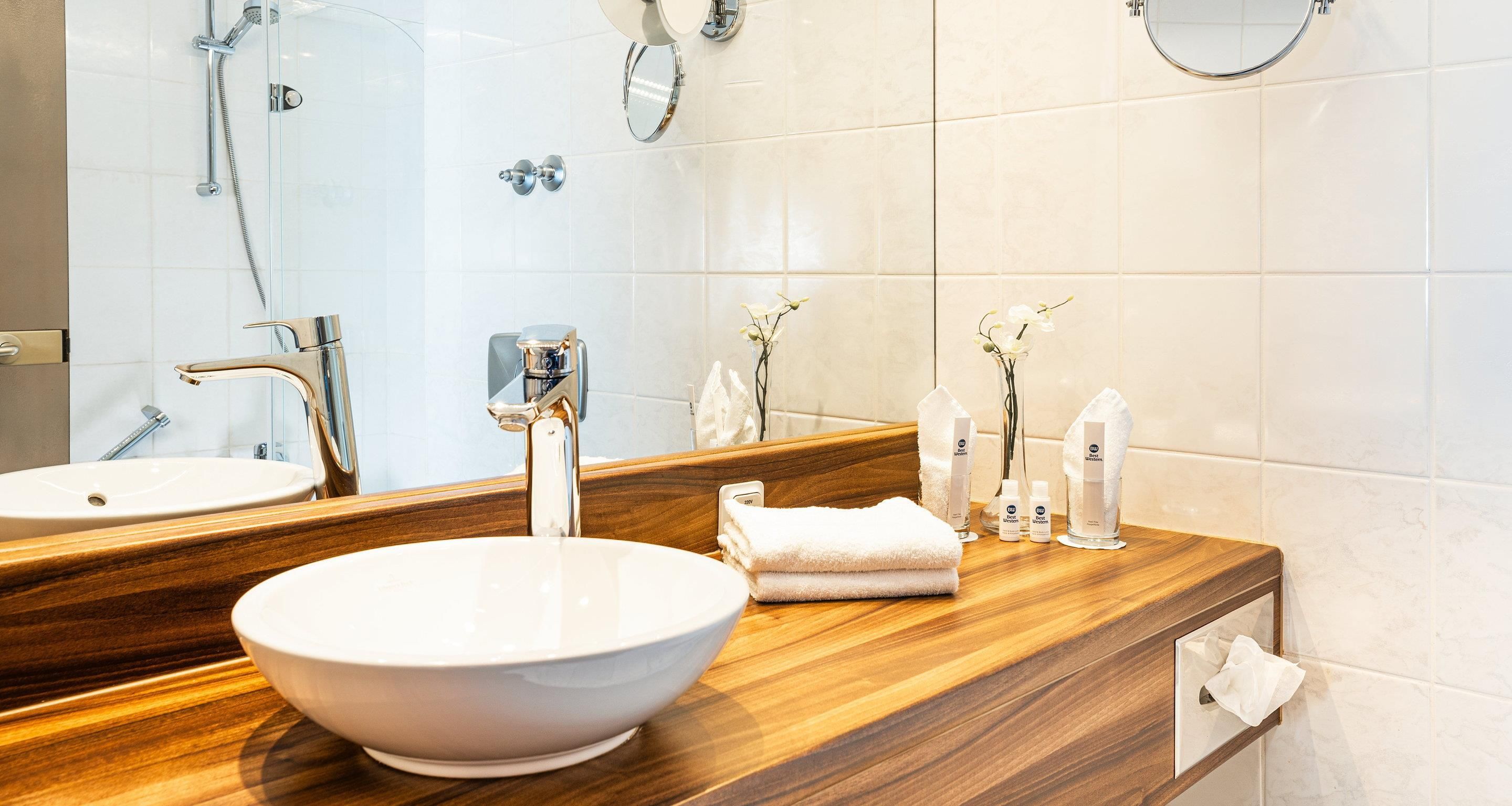A bathroom with a large mirror, a white sink, a wooden vanity, a shower, and a towel rack.
