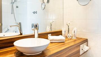 A bathroom with a large mirror, a white sink, a wooden vanity, a shower, and a towel rack.