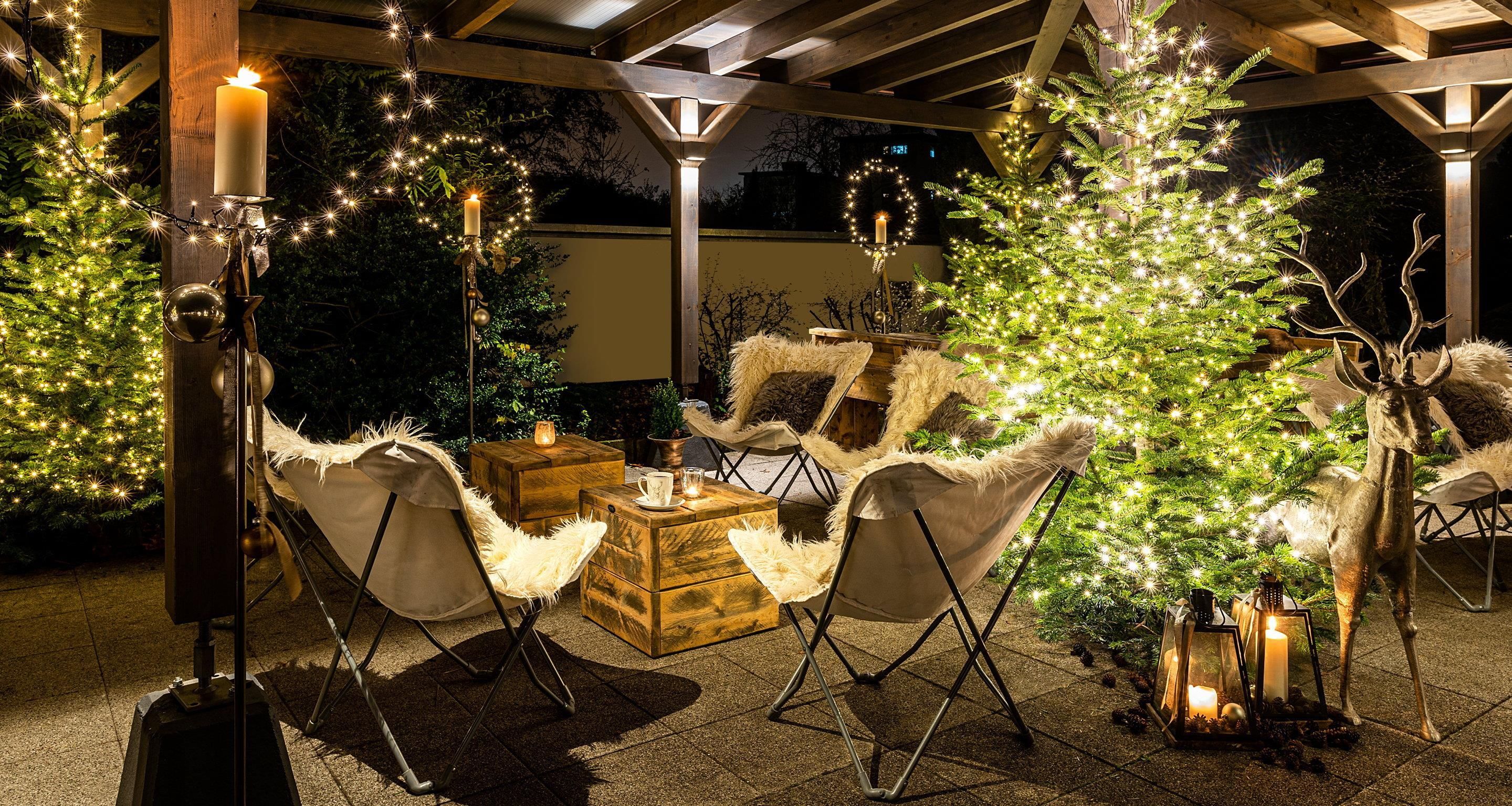 A cozy outdoor seating area with wooden furniture, a Christmas tree, and string lights.