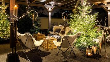 A cozy outdoor seating area with wooden furniture, a Christmas tree, and string lights.