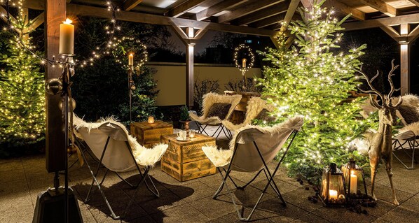 Un espacio al aire libre acogedor con muebles de madera, un árbol de Navidad y luces colgantes.