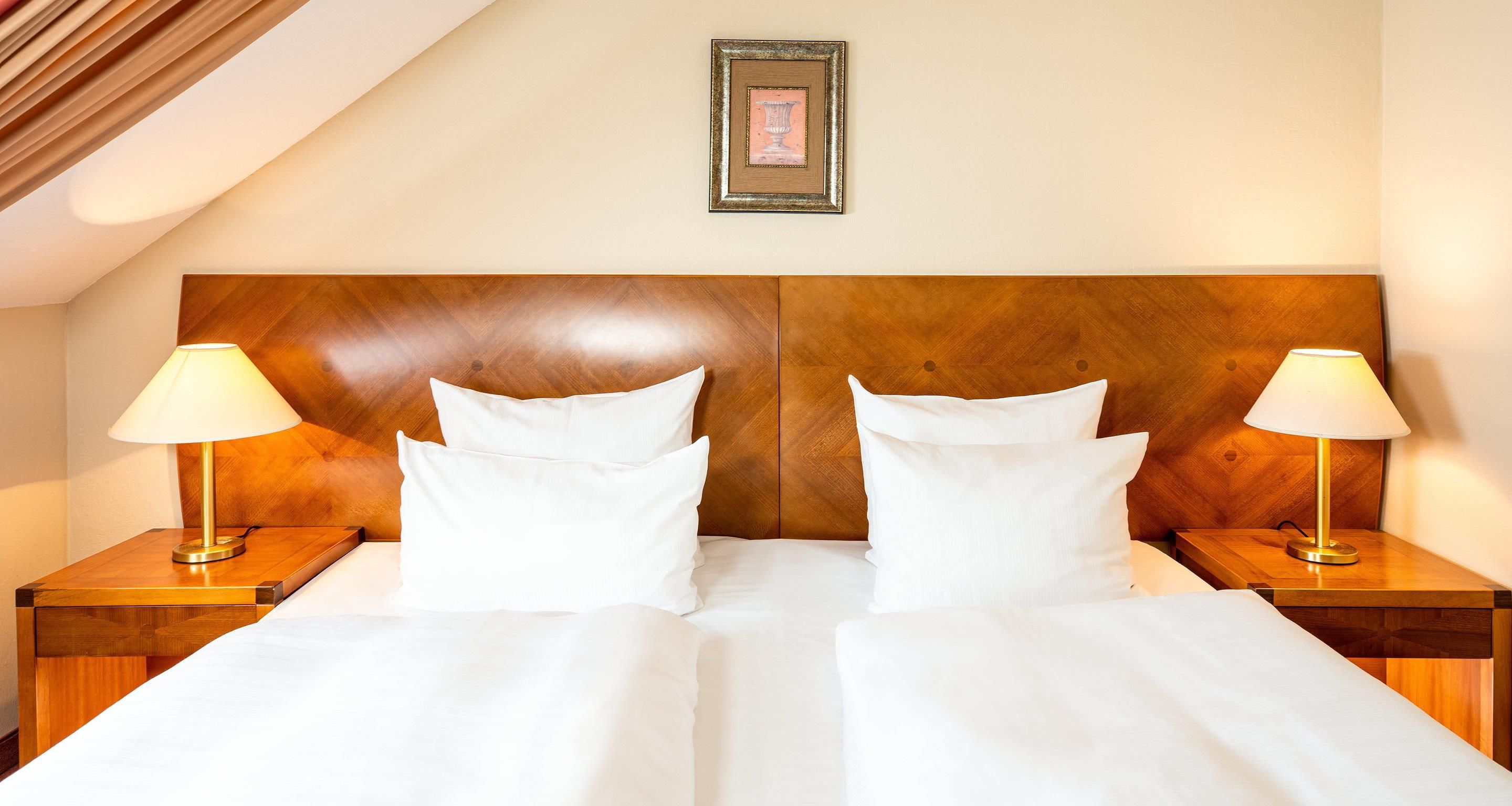 Una camera d'albergo con una testiera in legno, due lampade sui comodini e un quadro appeso al muro.