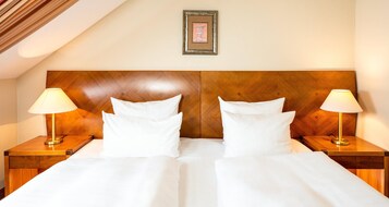 Una habitación de hotel con cabecera de madera, dos lámparas de noche y un cuadro en la pared.