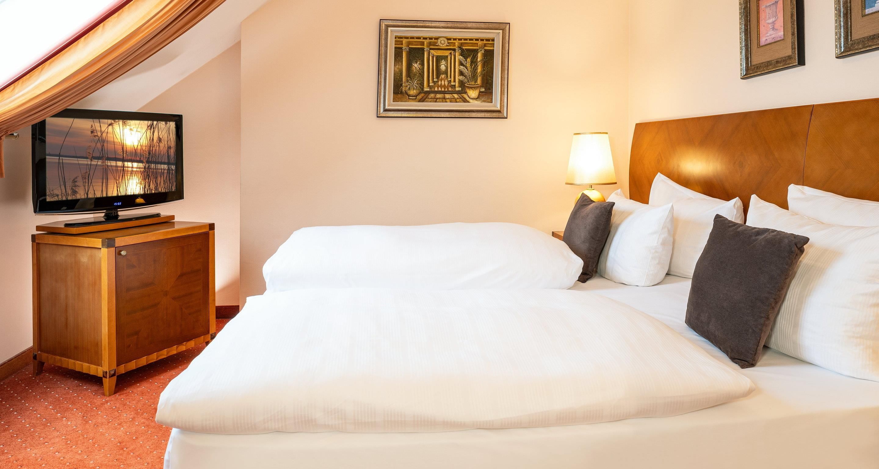 Ett hotellrum med en säng, en tv, en lampa och inramade konstverk på väggen.