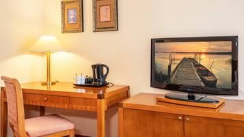 A wooden desk with a lamp, a chair, a coffee maker, and a television displaying a sunset scene.