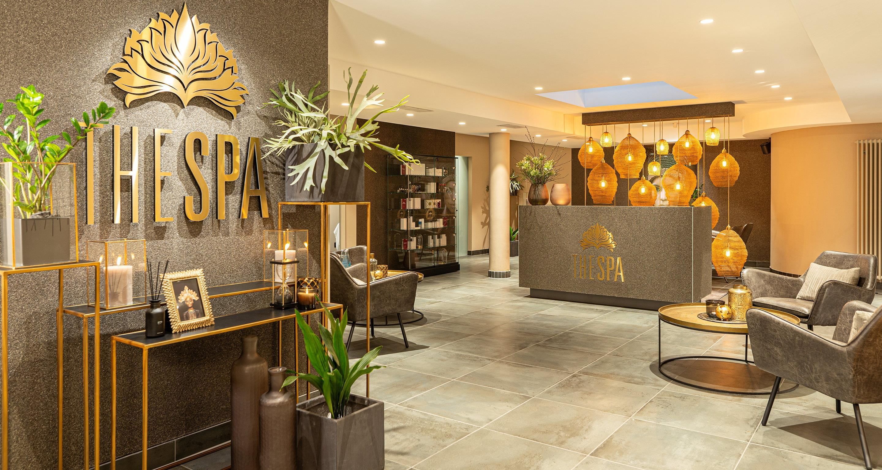A modern spa lobby with a reception desk, seating area, and decorative plants.