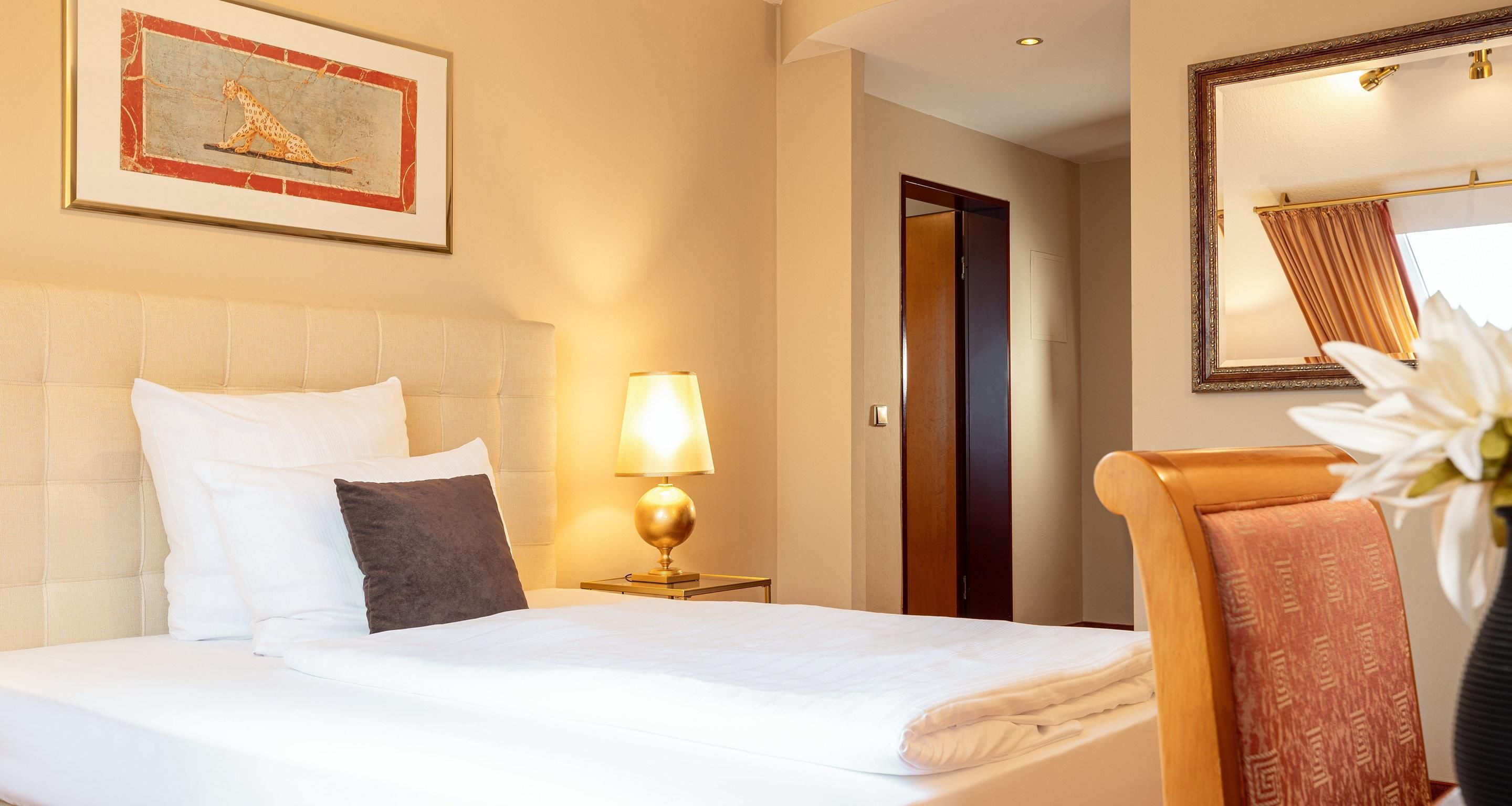 A hotel room with a bed, a nightstand with a lamp, a framed picture on the wall, a door, and a mirror.
