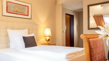 A hotel room with a bed, a nightstand with a lamp, a framed picture on the wall, a door, and a mirror.