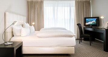Una habitación de hotel con cama, escritorio, silla, televisor y cortinas.