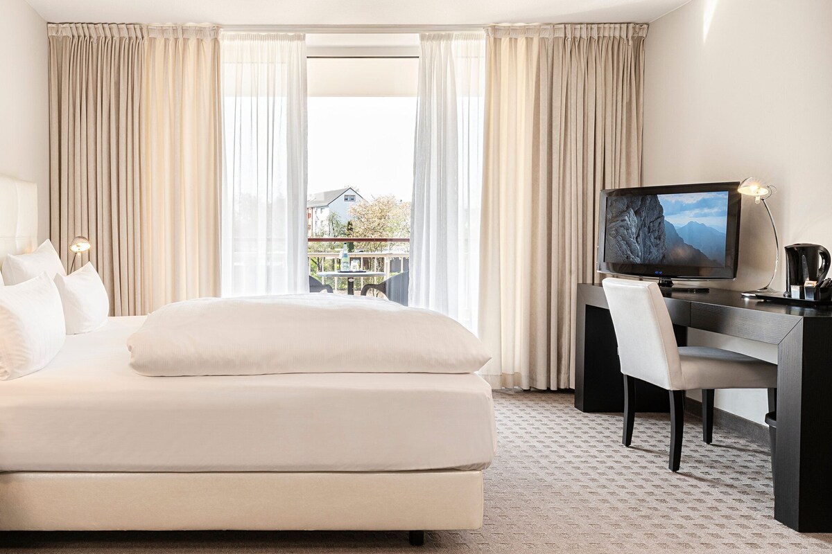 Habitación de hotel con cama, escritorio, silla, televisor y vista al exterior.