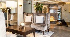 Un moderno vestíbulo con un sofá tapizado gris, una mesa de centro de madera y una planta grande en maceta.