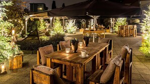 An outdoor dining area with wooden tables and chairs, surrounded by illuminated trees and plants. - Best Western Victor's Residenz-Hotel Rodenhof (Saarbrücken)