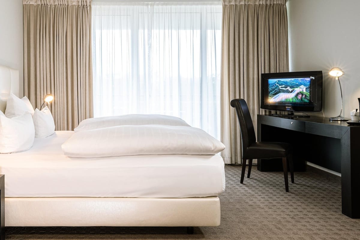A hotel room with a bed, a desk, a chair, a TV, and curtains.
