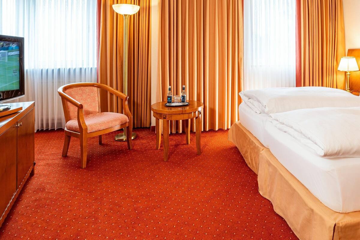 A hotel room with a bed, a chair, a small table with a tray, a TV, and curtains.