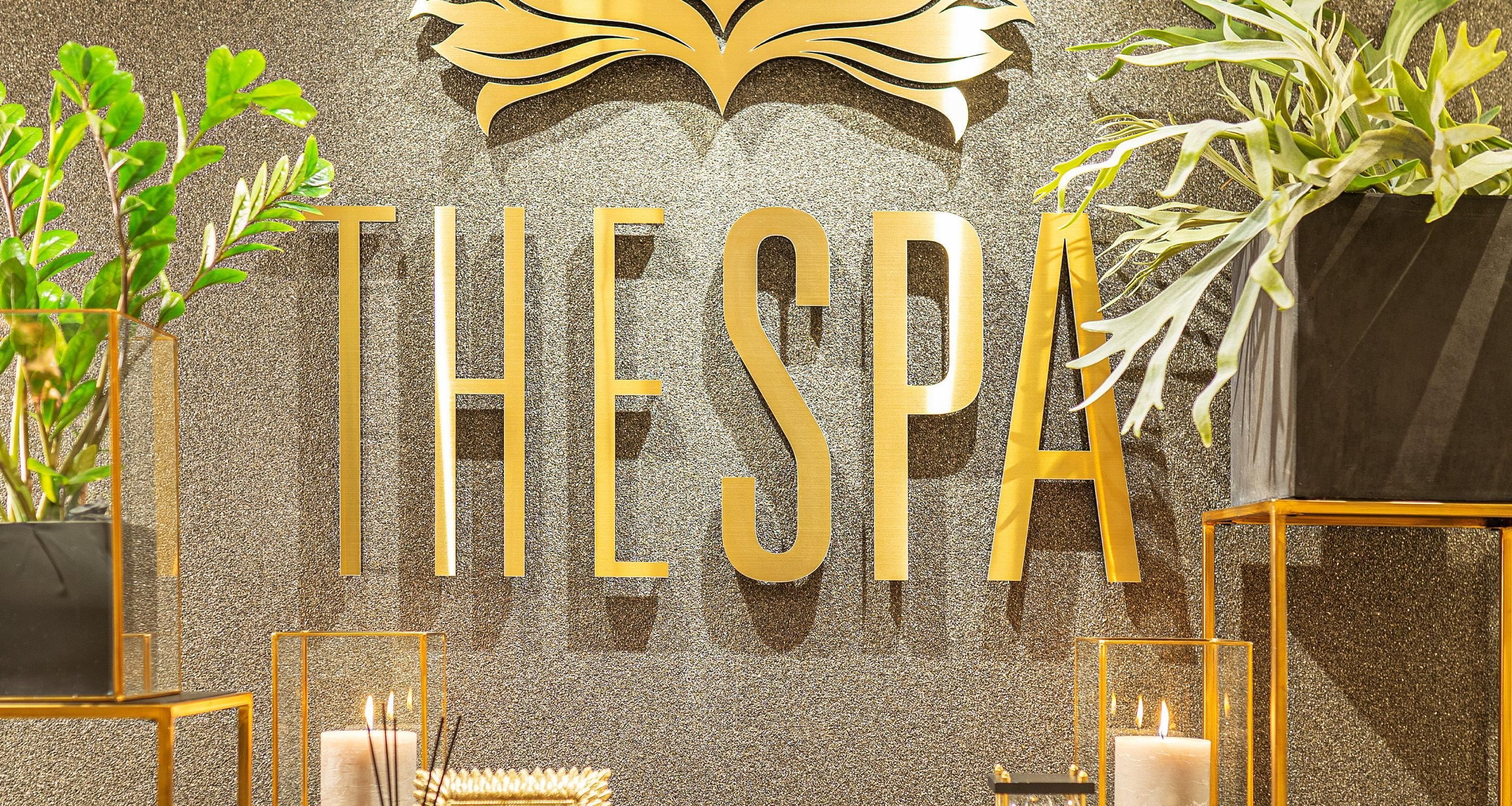 A spa with gold lettering on a textured wall, potted plants, and candles.